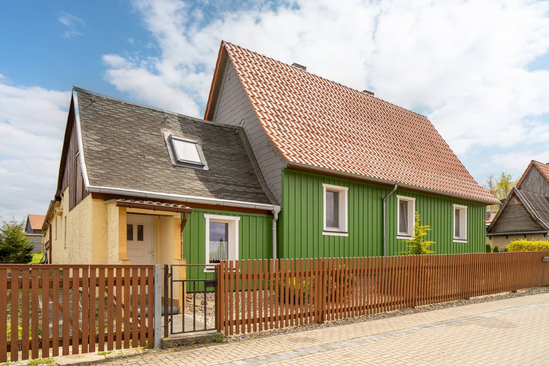 Ferienhaus am Osterberg in Allrode – grünes Ferienhaus mit rotem Dach und eingezäuntem Garten unter blauem Himmel